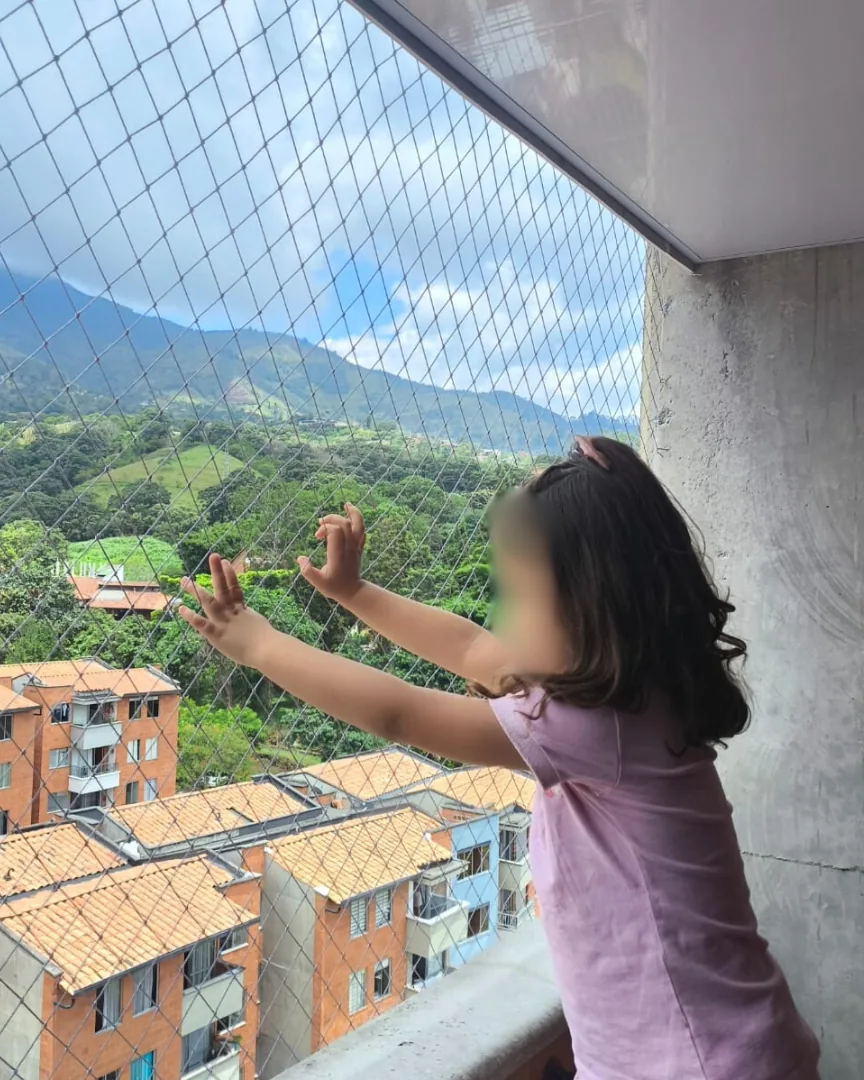 Niña apoyada en malla de seguridad en balcón de apartamento